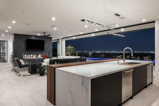 kitchen featuring a spacious island, sink, pendant lighting, ceiling fan, and light stone countertops