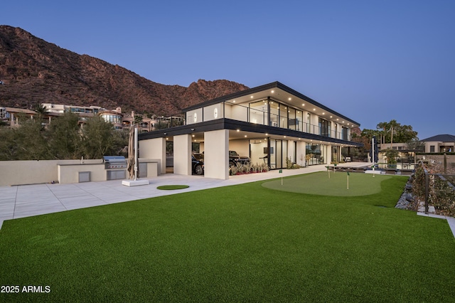 back house at dusk with a balcony, an outdoor kitchen, a mountain view, and a patio