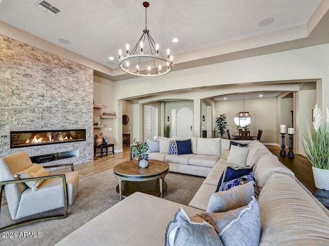 living room featuring a chandelier, a stone fireplace, hardwood / wood-style flooring, and a tray ceiling