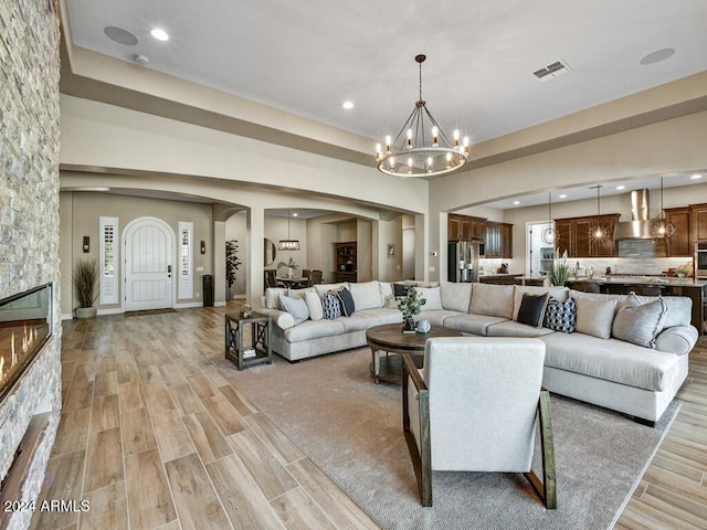 living room featuring a stone fireplace, a chandelier, and light hardwood / wood-style floors