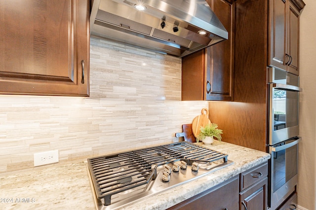 kitchen with tasteful backsplash, appliances with stainless steel finishes, wall chimney exhaust hood, and light stone countertops