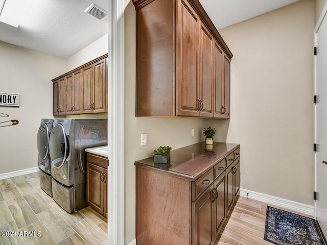 clothes washing area with washer and dryer, light hardwood / wood-style floors, and cabinets