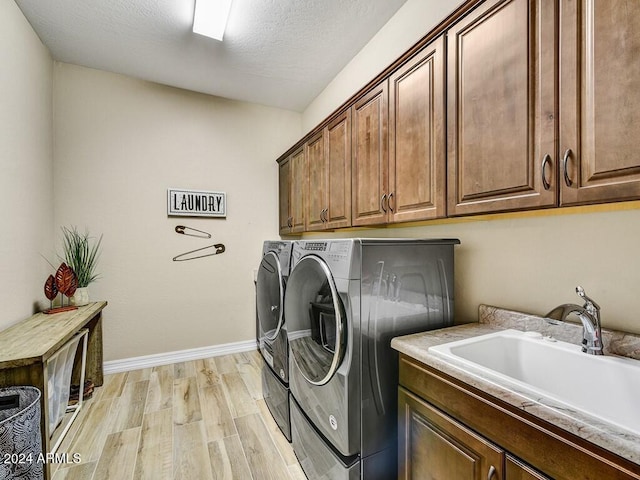 washroom featuring sink, light hardwood / wood-style flooring, cabinets, a textured ceiling, and washing machine and clothes dryer