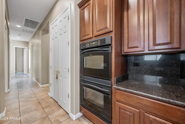 kitchen featuring double oven, dark stone countertops, decorative backsplash, and light tile patterned flooring