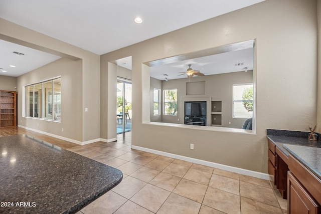 kitchen featuring ceiling fan, light tile patterned flooring, and dark stone countertops