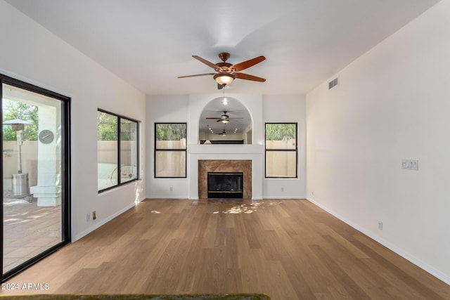 unfurnished living room with a premium fireplace, a ceiling fan, visible vents, baseboards, and light wood finished floors