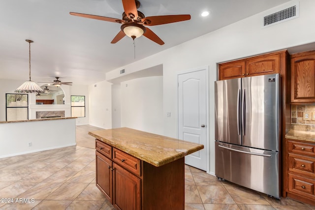 kitchen with visible vents, brown cabinetry, a kitchen island, decorative light fixtures, and freestanding refrigerator