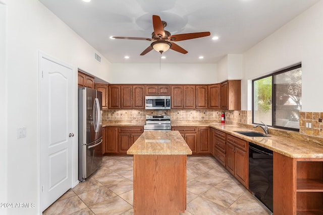 kitchen featuring brown cabinetry, a center island, light stone countertops, stainless steel appliances, and a sink