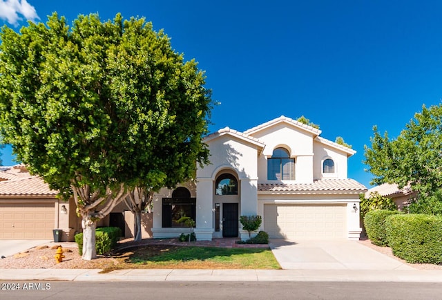 mediterranean / spanish-style house with a garage, concrete driveway, a tile roof, and stucco siding