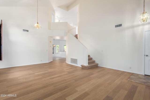 unfurnished living room with light wood-style flooring, stairway, a high ceiling, and visible vents