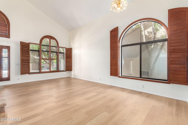 unfurnished room with high vaulted ceiling, an inviting chandelier, light wood-style flooring, and baseboards