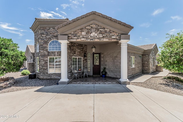 view of front facade with a tiled roof, stone siding, and covered porch