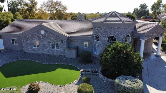 view of front of property featuring a chimney, a tile roof, and stone siding