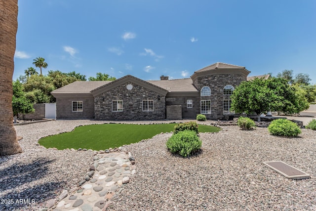 view of front of house with fence, a tile roof, and stone siding