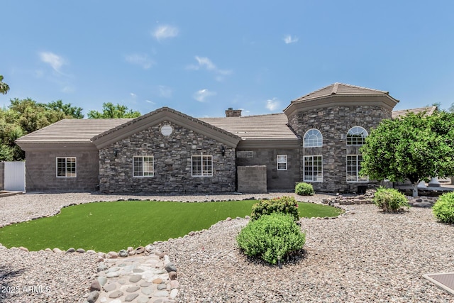 view of front facade featuring a tiled roof, a chimney, a front lawn, and stone siding
