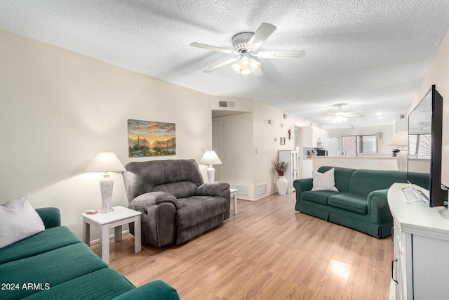 living area featuring light wood finished floors, ceiling fan, visible vents, and a textured ceiling