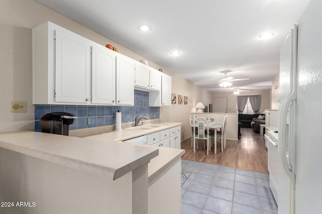 kitchen with a peninsula, white appliances, a sink, white cabinetry, and light countertops