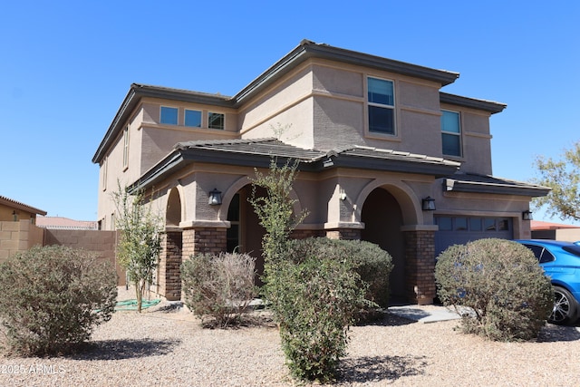 view of front of house with stone siding, fence, an attached garage, and stucco siding