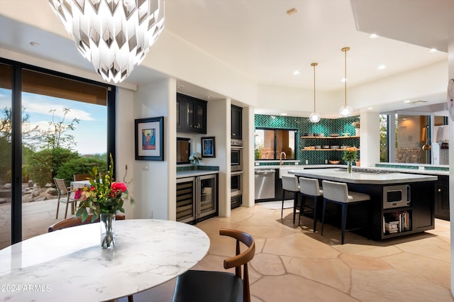 kitchen featuring backsplash, stainless steel appliances, beverage cooler, pendant lighting, and a kitchen island with sink