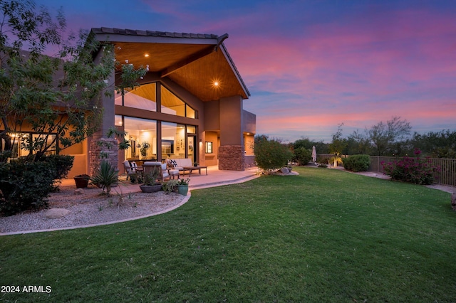 back house at dusk featuring a yard and a patio