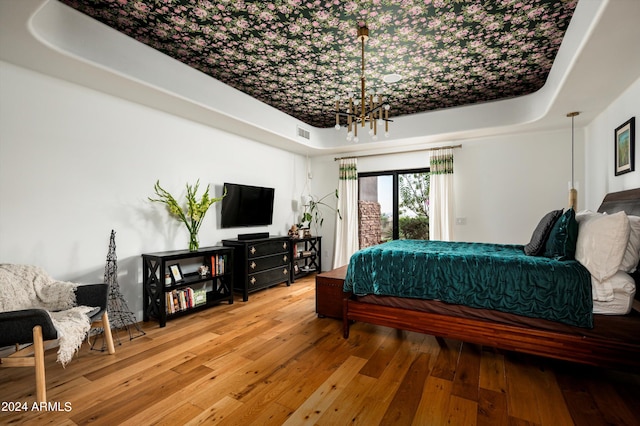 bedroom with hardwood / wood-style floors, a tray ceiling, and a notable chandelier