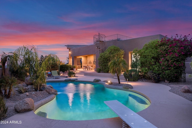 pool at dusk with a diving board and a patio area