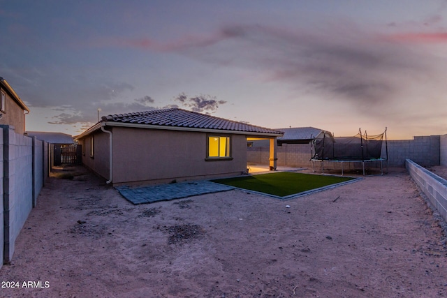 back house at dusk with a trampoline and a patio area