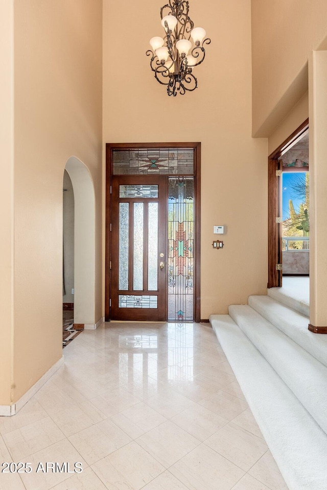 entrance foyer with a chandelier, arched walkways, a high ceiling, and baseboards