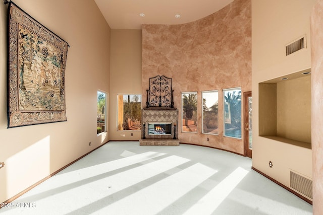 unfurnished living room featuring carpet flooring, a fireplace, visible vents, and a towering ceiling