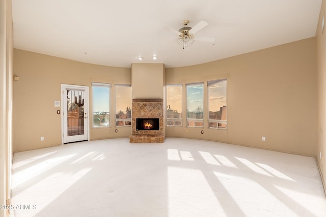 unfurnished living room featuring light carpet, a lit fireplace, and a ceiling fan