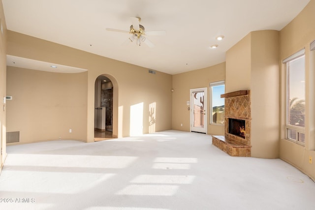 carpeted living area featuring ceiling fan, visible vents, arched walkways, and a premium fireplace