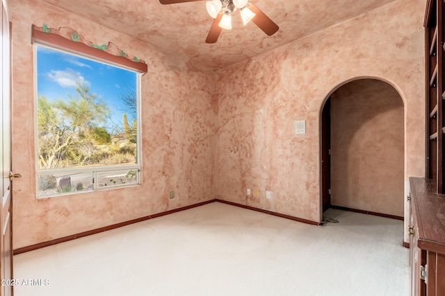 empty room featuring baseboards, arched walkways, carpet, and ceiling fan