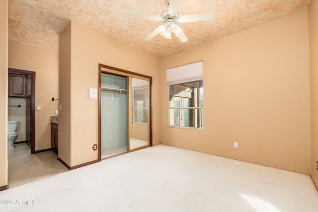 unfurnished bedroom featuring baseboards, ensuite bath, ceiling fan, a closet, and light colored carpet