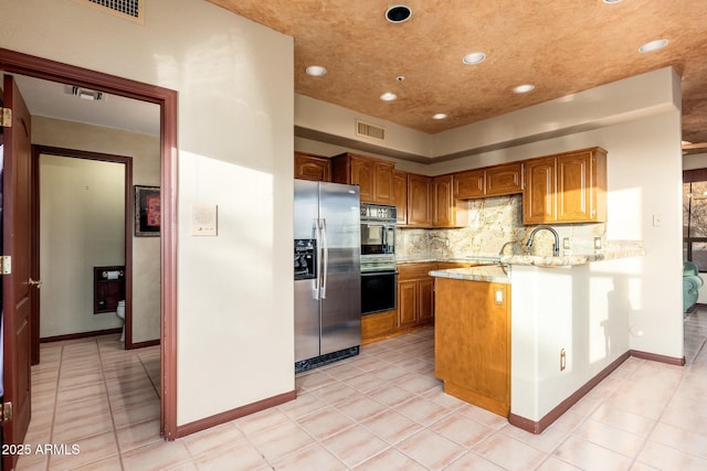 kitchen featuring light stone counters, visible vents, a peninsula, decorative backsplash, and stainless steel fridge