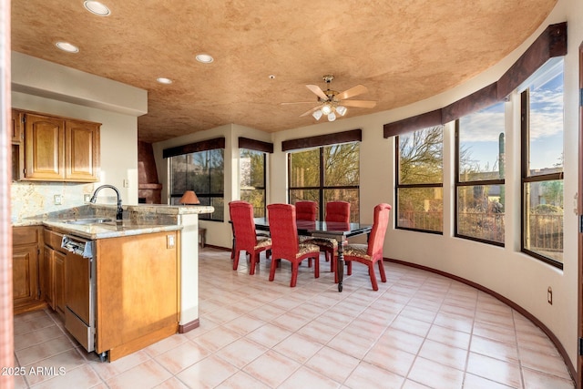 kitchen with a ceiling fan, light stone countertops, a peninsula, a sink, and stainless steel dishwasher