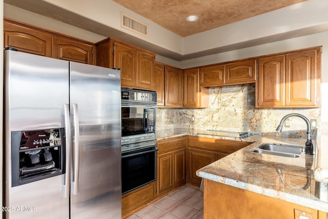 kitchen with brown cabinetry, visible vents, black appliances, and a sink