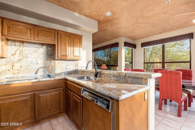 kitchen featuring a sink, brown cabinets, dishwasher, and a peninsula