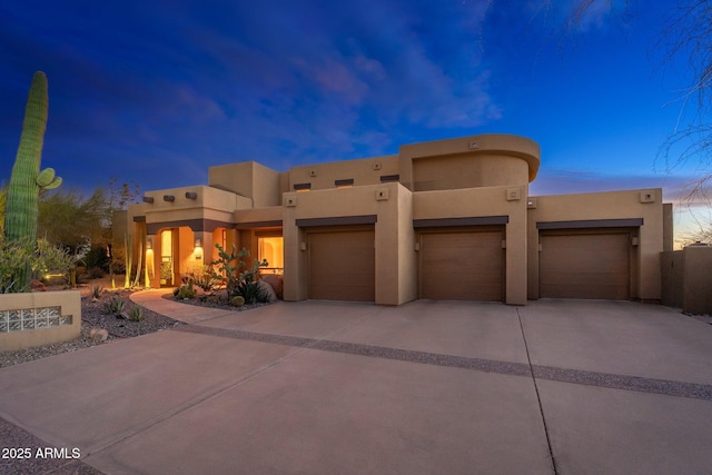 pueblo revival-style home with stucco siding, an attached garage, and concrete driveway