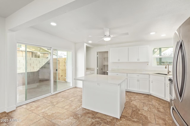 kitchen with sink, stainless steel fridge, ceiling fan, white cabinets, and a kitchen island