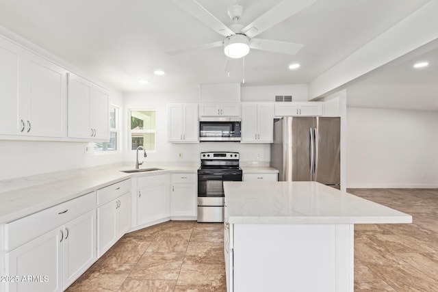 kitchen featuring appliances with stainless steel finishes, white cabinetry, sink, a center island, and light stone countertops