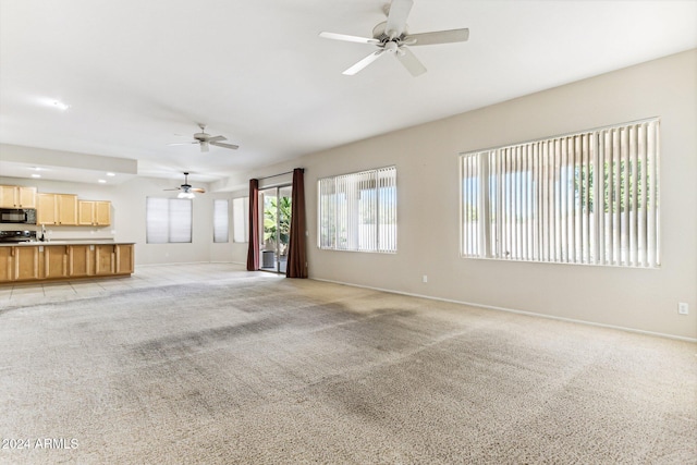 unfurnished living room featuring light colored carpet, sink, and ceiling fan