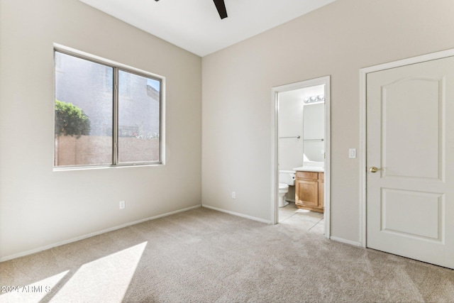 unfurnished bedroom featuring ensuite bathroom, light colored carpet, and ceiling fan