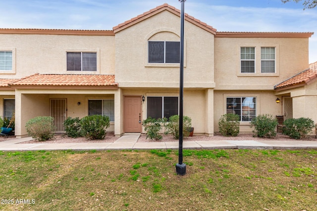 townhome / multi-family property featuring stucco siding, a tiled roof, and a front lawn