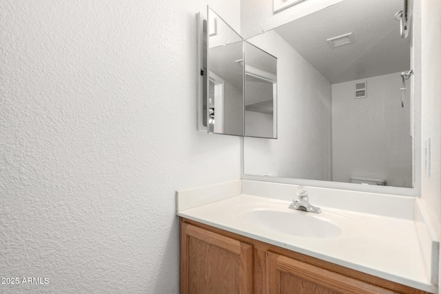 bathroom with visible vents, vanity, and a textured wall