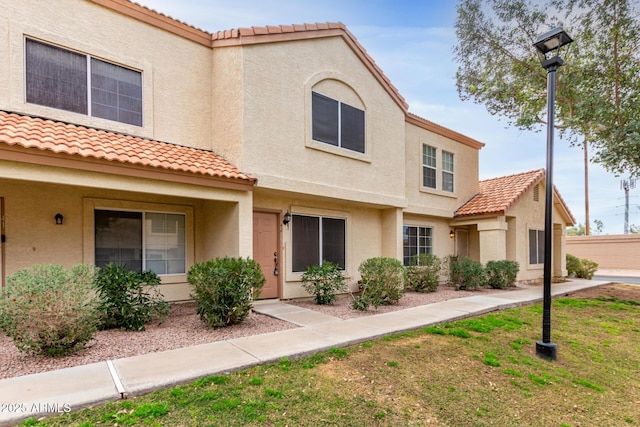 townhome / multi-family property with stucco siding, a front lawn, and a tiled roof