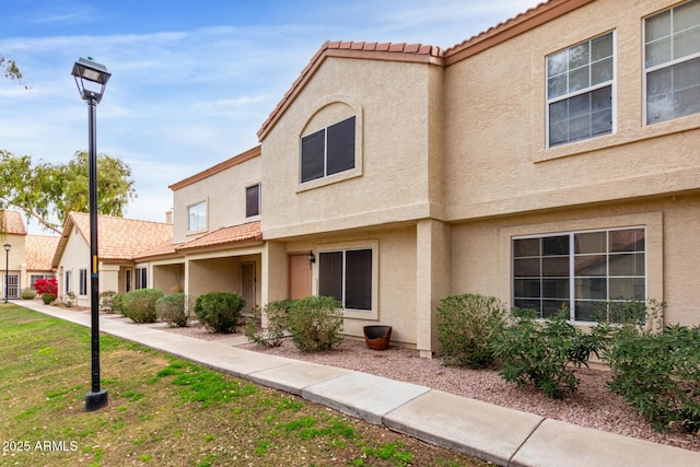 view of property featuring stucco siding, a front yard, and a tiled roof