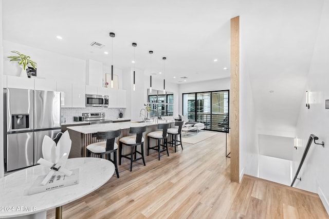 kitchen with visible vents, a center island with sink, a kitchen bar, white cabinetry, and appliances with stainless steel finishes