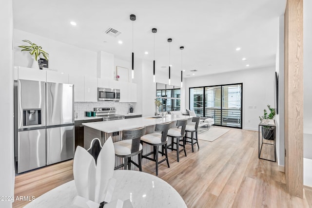 kitchen with white cabinets, light wood-style floors, stainless steel appliances, visible vents, and modern cabinets