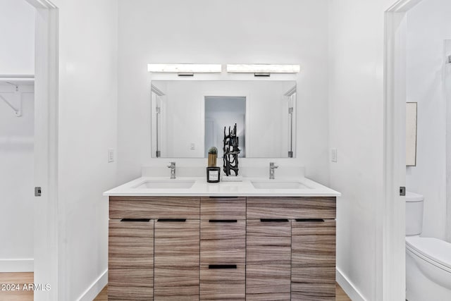 bathroom featuring double vanity, toilet, baseboards, and a sink