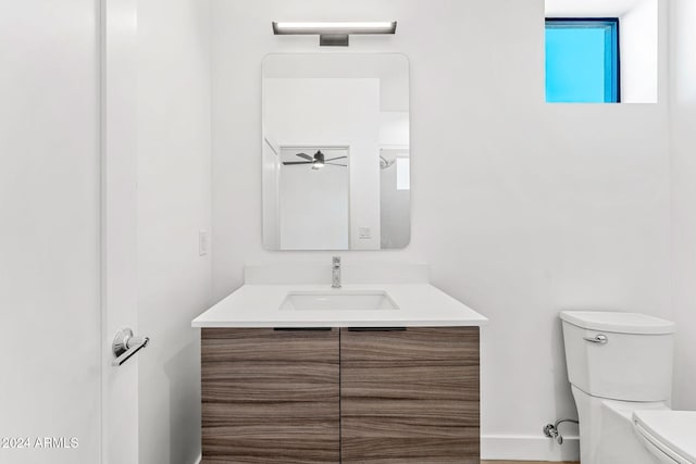 half bath with vanity, a ceiling fan, and toilet